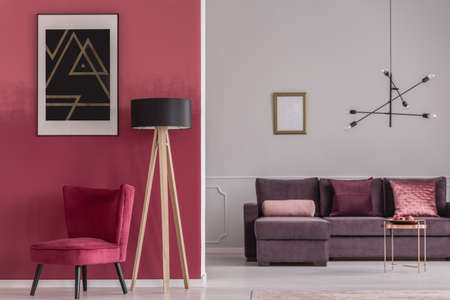 Black poster on red wall above armchair and wooden lamp in open space interior with mockupの写真素材