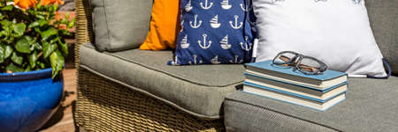Close-up of books, glasses and colorful pillows on a wicker sofa on a stylish designed terraceの写真素材