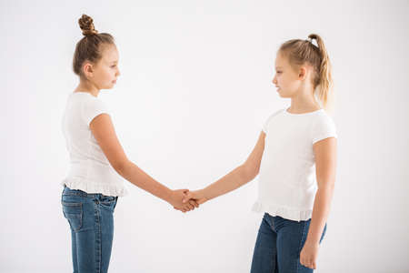 Blonde girls shaking hands after a fight, standing against white backgroundの写真素材