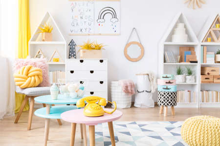 Yellow phone on pink, round table in scandi child's playroom interior with poster on the wallの写真素材