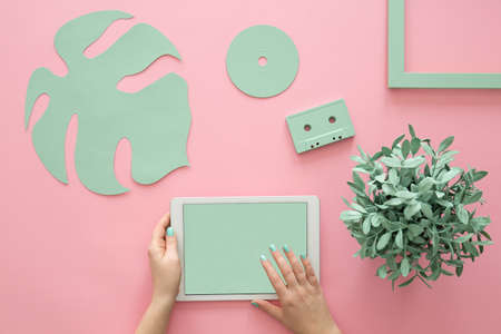 Top view of a plant and mint green objects arrangement on a rose quartz background and female hands holding a tabletの写真素材