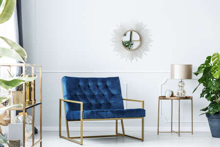 Navy blue armchair next to gold table with lamp against white wall with mirror in living room interiorの写真素材