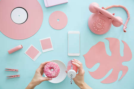 View from above on female hands holding a pink smoothie and doughnut on a pale blue background with rose quartz conceptual objectsの写真素材