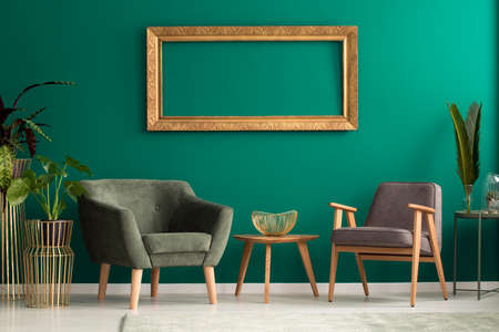 Elegant fruit bowl on a wooden table between retro armchairs with wooden legs in a luxurious, green...