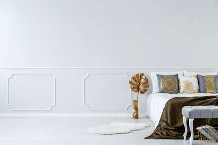 Gold leaf next to bed in modern bedroom interior with copy space on white wall with moldingの写真素材