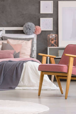 Retro armchair standing on white, wooden floors in a gray and pastel girly bedroom interiorの写真素材