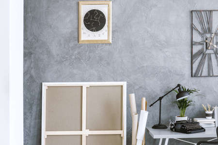 Poster and clock on concrete wall in workspace interior with black lamp and typewriter on the deskの写真素材