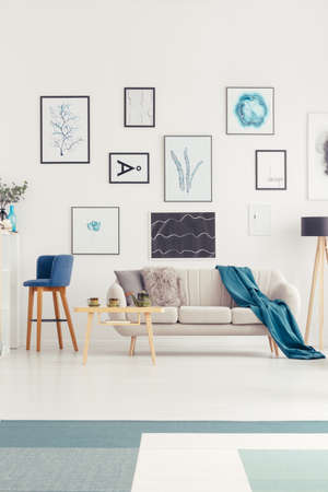 Art gallery on the wall, white sofa and blue bar stool in a living room interior