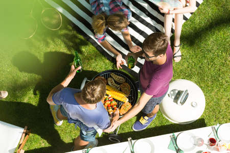 Two guys standing next to a barbecue and drink while meeting in the parkの写真素材