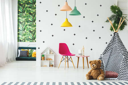 Plush toy next to tent in scandinavian child's room interior with pink chair under colorful lampsの写真素材