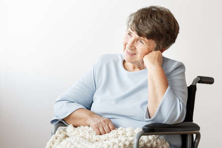 Satisfied, disabled senior woman sitting in a wheelchair and watching her grandkidsの写真素材