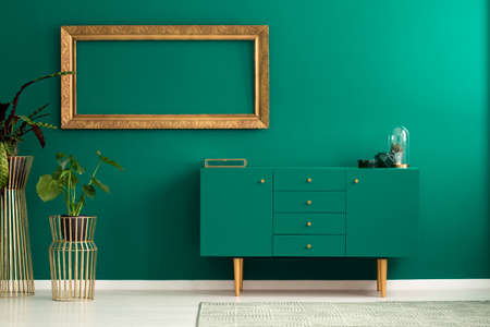 Cactus in a glass dome on a modern sideboard with wooden legs in a green living room interior with golden decorationsの写真素材