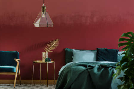 Double bed with emerald sheets and gold side table with leaf decoration in bedroom interior