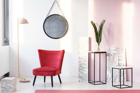 Sitting area with maroon armchair, lamp, mirror, marble cubes and metal stools