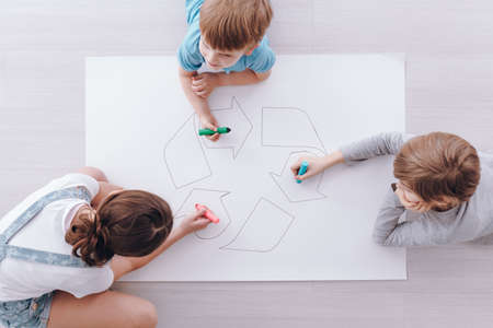 Kids sitting on the floor and drawing a poster of recycling signの写真素材