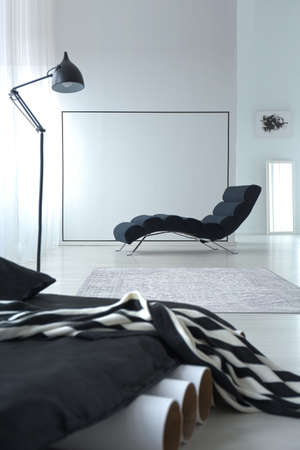Close-up of a black mattress on tubes with chaise lounge and lamp in the background in bedroom...