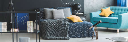 Yellow star pillow on turquoise armchair near telescope in cozy bedroom interior with knit blanket on bedの写真素材