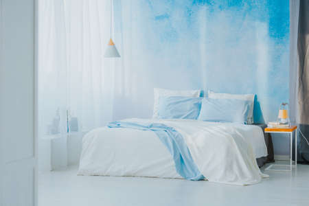 Side angle of king size bed next to a wooden side table and blue wallpaper decoration
