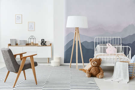 Grey armchair and wooden lamp on carpet in child's bedroom interior with plush toy and mountain wallpaperの写真素材