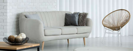 Bright grey sofa with decorative cushions standing in a living room interior with white brick wall and golden chairの写真素材