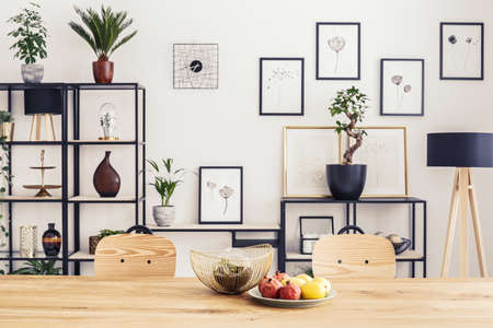 Wooden chairs at table with fruits in dining room interior with plants and posters on the wallの写真素材