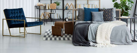 Bed with many pillows and three blankets standing in the middle of a bright room interior with dark...
