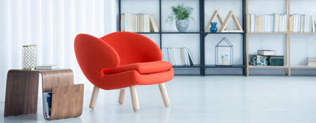 Modern, wooden table standing by an orange chair in bright sitting room interiorの写真素材