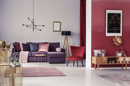 Spacious, maroon apartment interior with corner sofa, red armchair and wooden cupboardの写真素材