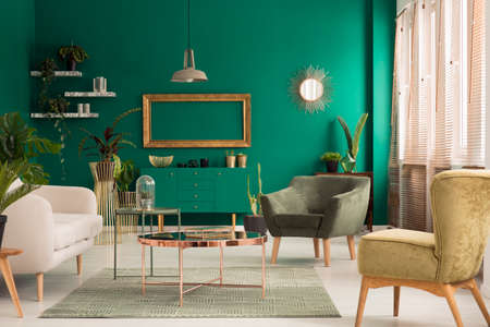 Copper table on rug and gold frame in living room interior with green armchair and beige sofaの写真素材