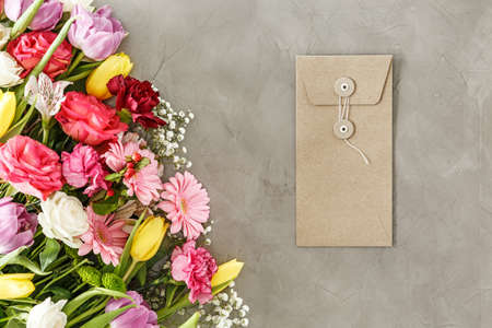 Brown envelope for a greeting card lying on a gray table next to a bouquet of flowers for mother's dayの写真素材