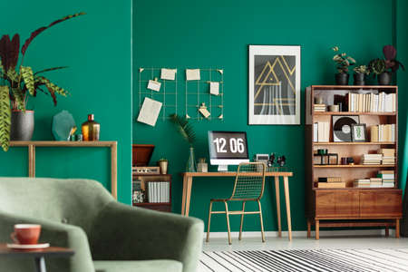 Green living room interior with books on wooden cupboard and desk for remote work