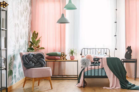 Pink chair with handmade, grey knot cushion placed in bright bedroom interior for a teenage girlの写真素材