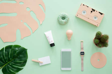 Pink cassette, smartphone and watch on mint background with green leafの写真素材