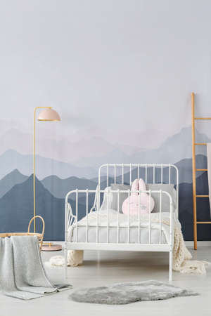 Simple, pastel pink lamp standing in bright children bedroom interior with mountain wallpaper and white bedの写真素材