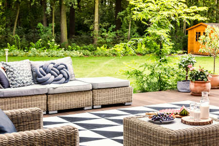 Knot pillow on rattan couch on a patio with table surrounded by green grass
