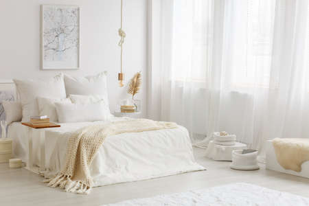 Warm, white and gold bedroom interior with beige blanket on white sheets of the bed