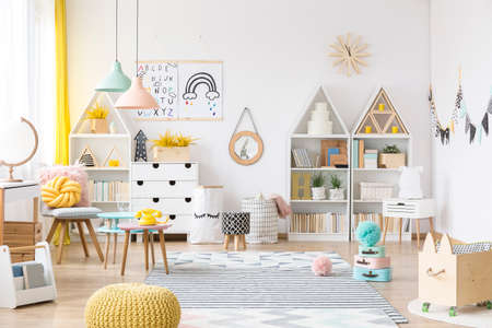 Pastel lamps above a table in spacious child's room interior with yellow pouf and wooden boxの写真素材