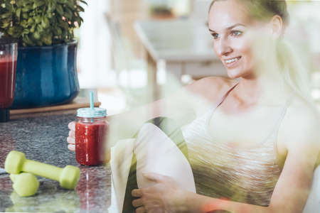 Young woman sitting by the table and drinking smoothie after morning workout routine