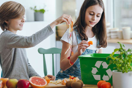 Girl and boy trowing out fruits waste into green recycling containerの写真素材