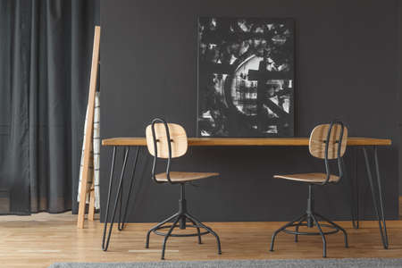 Black and white painting standing against a dark wall, on a wooden dining table in monochromatic room interiorの写真素材
