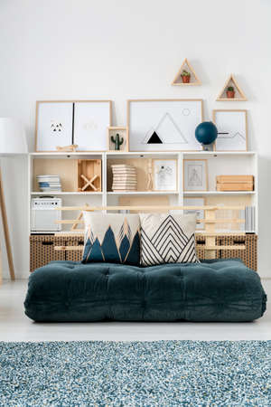 Simple living room interior with green futon instead of a sofa and posters on bookcases against white wallの写真素材
