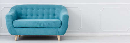 Turquoise couch standing in an empty, light grey room interior in a photo with copy spaceの写真素材