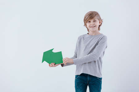 Smiling boy with green arrow against white background with copy spaceの写真素材