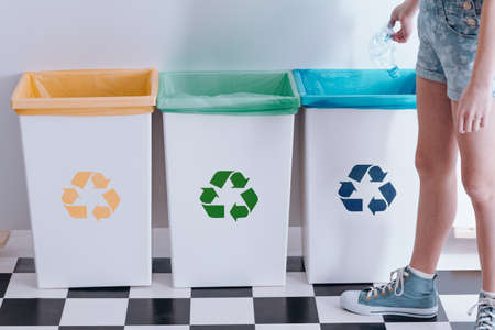Kid throwing out a plastic bottle into a blue bin. Child recycling education concept