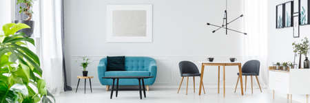 Two coffee cups on a wooden table in white living room interior with blue couch and silver painting...