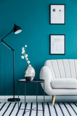White flowers on table between sofa and lamp in blue living room interior with postersの写真素材