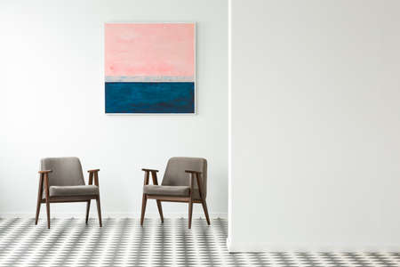 Pastel painting on white wall above grey armchairs in interior with checkerboard floor