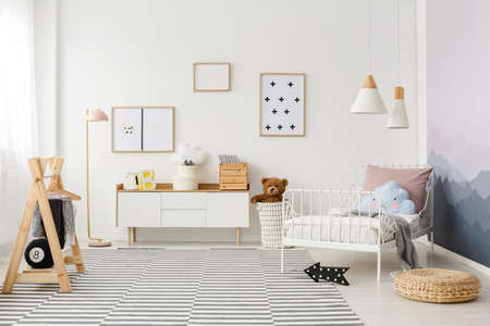 Simple posters hanging on the wall in white children bedroom interior with striped carpet, metal bed and wooden furnitureの写真素材