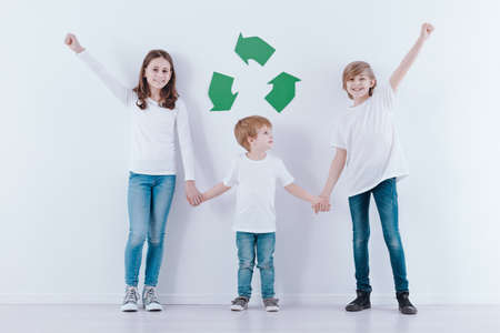 Children holding hands against white background with green symbol of recyclingの写真素材