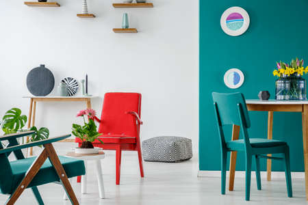 Blue and red chair at table with flowers in living room interior with plates on a green wallの写真素材